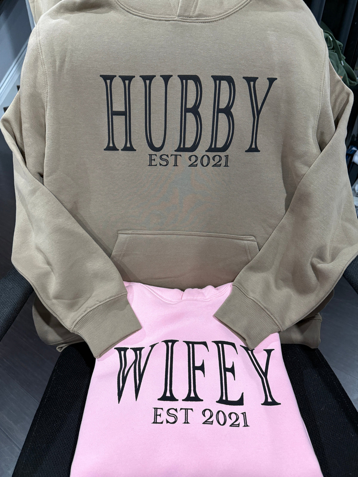 Matching tan "Hubby Est 2021" hoodie and pink "Wifey Est 2021" custom printed hoodies from Must Be Nice